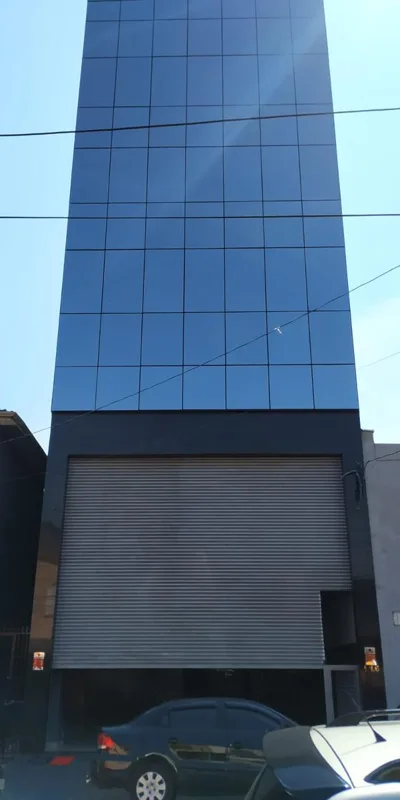 Fachada estreita com revestimento de vidro azul e acesso no térreo.