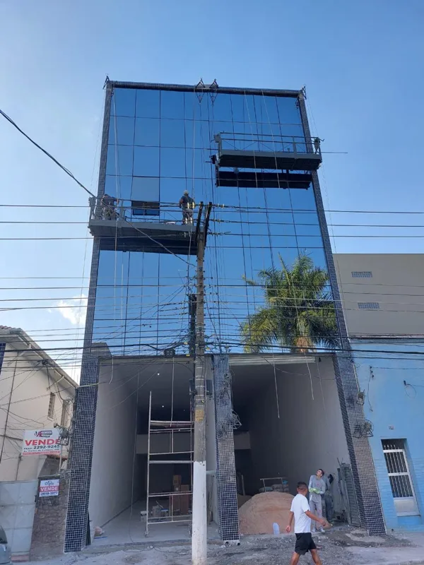 Edificação com fachada de vidro azul e equipamentos de trabalho em altura.